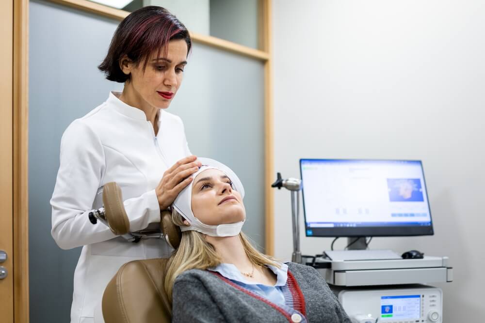 Adult female psychiatrist is placing a transcranial magnetic stimulation device on a young girl