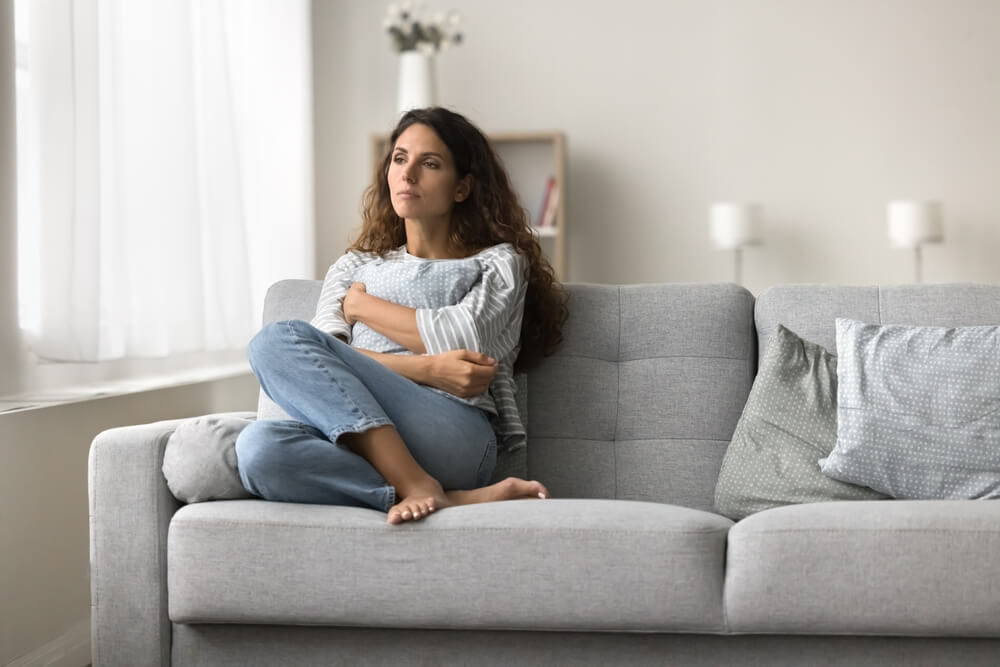 Sad lonely young woman sitting on couch at home