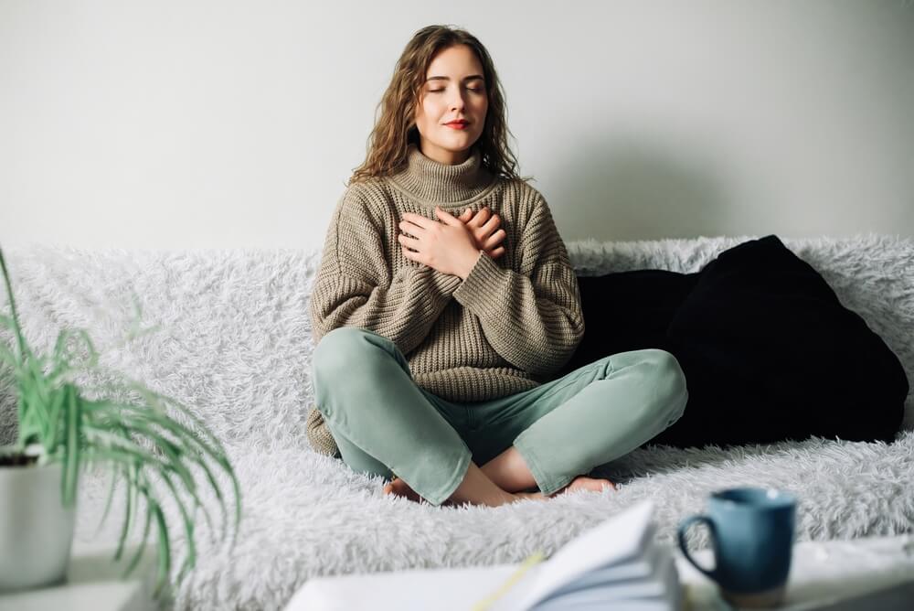 Woman practicing pranayama in lotus position on bed, breathing exercises to reduce stress