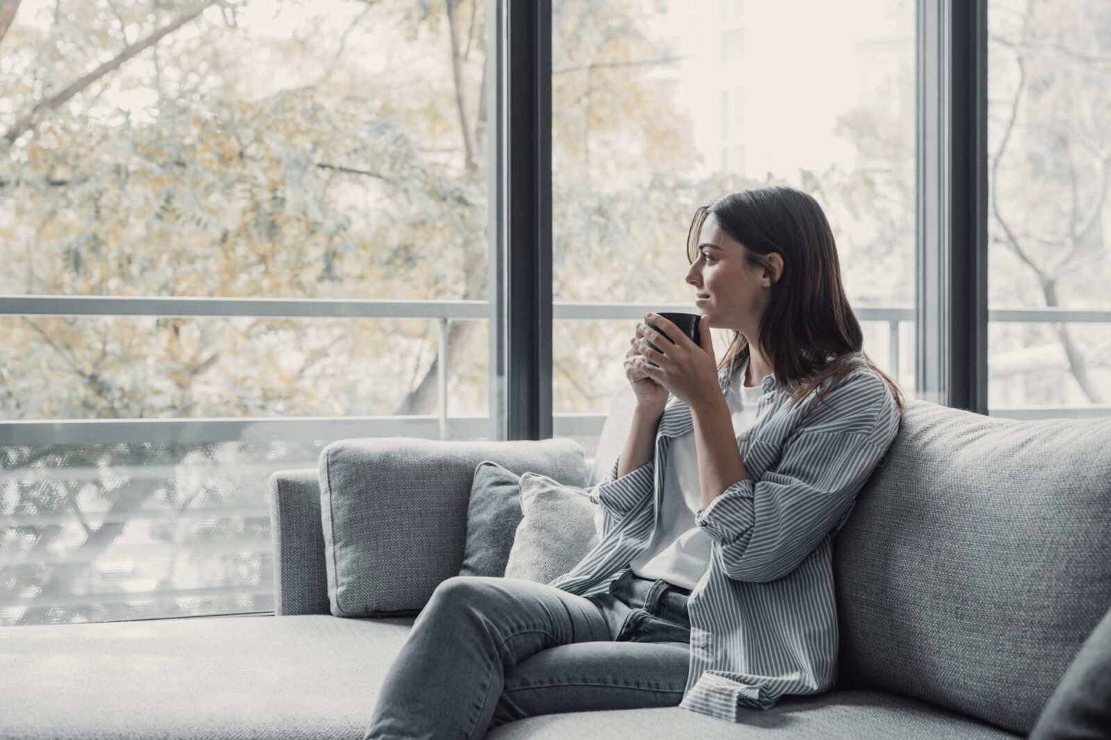 Cheerful dreamy girl holding mug of hot beverage, looking away