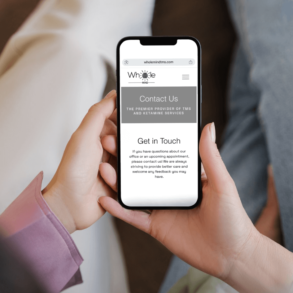 Hands holding smartphone with Whole Mind contact info