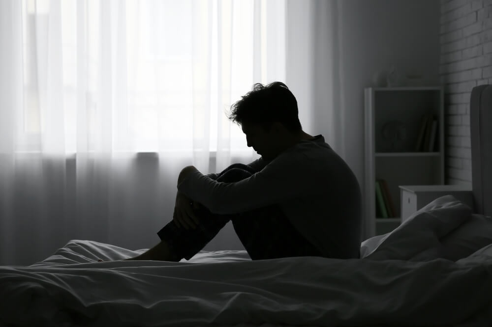 Depressed young man sitting in dark bedroom