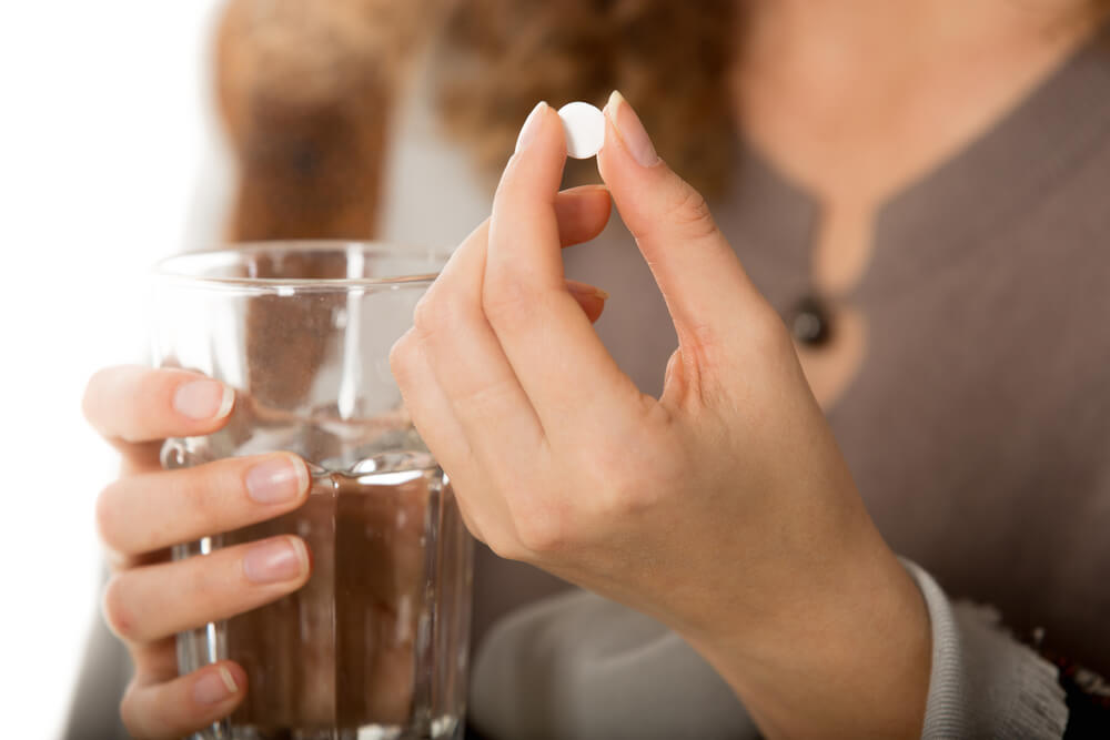 Female hands holding one white round pill and glass of water