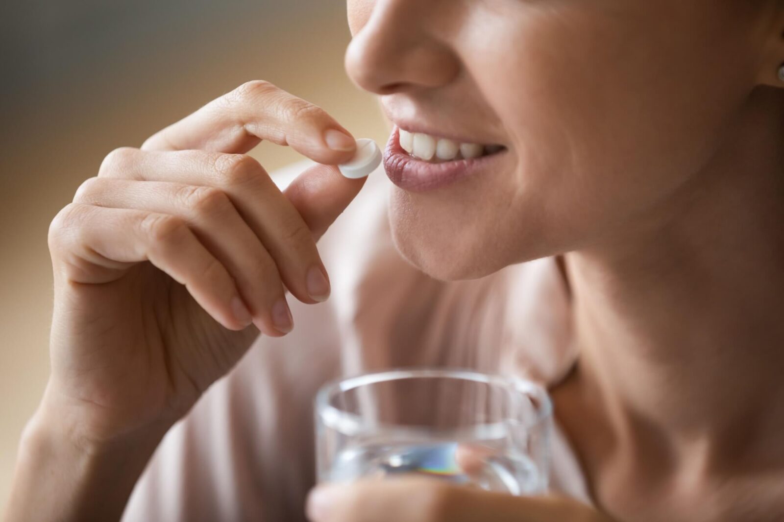 Smiling attractive woman holding white round pill and glass of water,