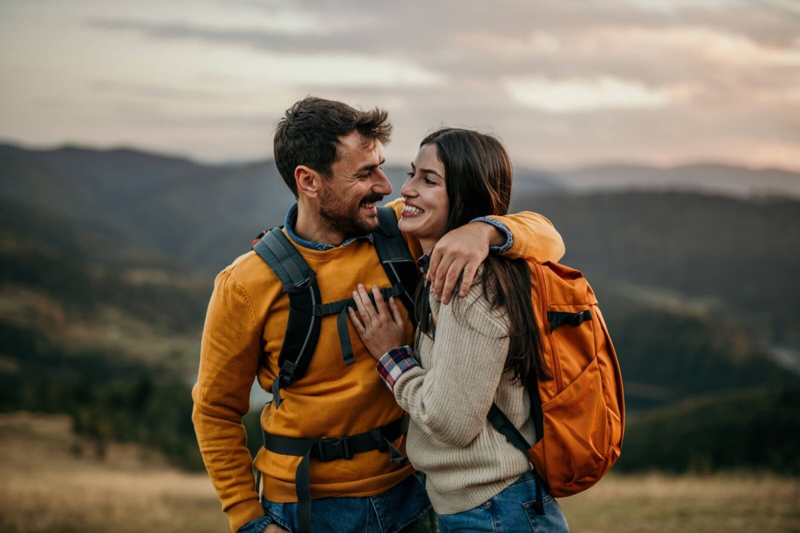 Couple walking uphill with backpacks, catching sight of a serene lake