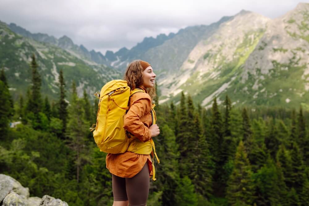 Active woman tourist with backpack enjoys the beautiful scenery of the majestic mountains