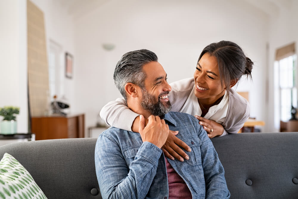 Smiling woman hugging her husband on the couch from behind