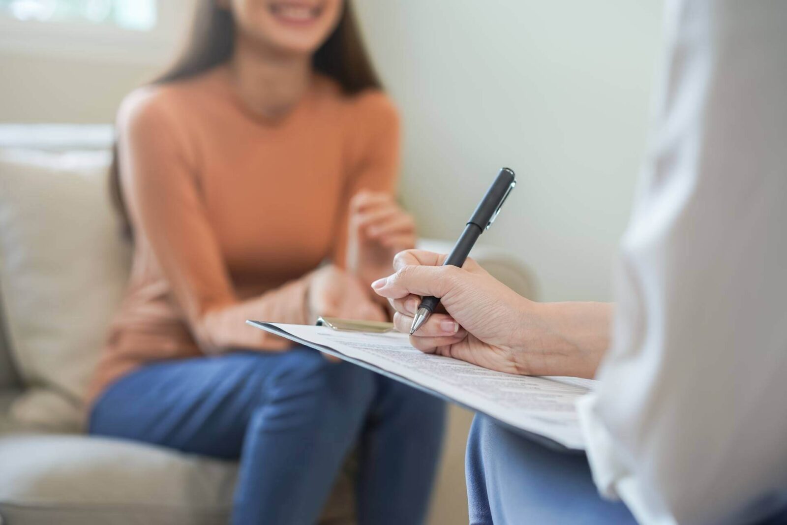 smiling young woman explaining symptom while doctor taking notes