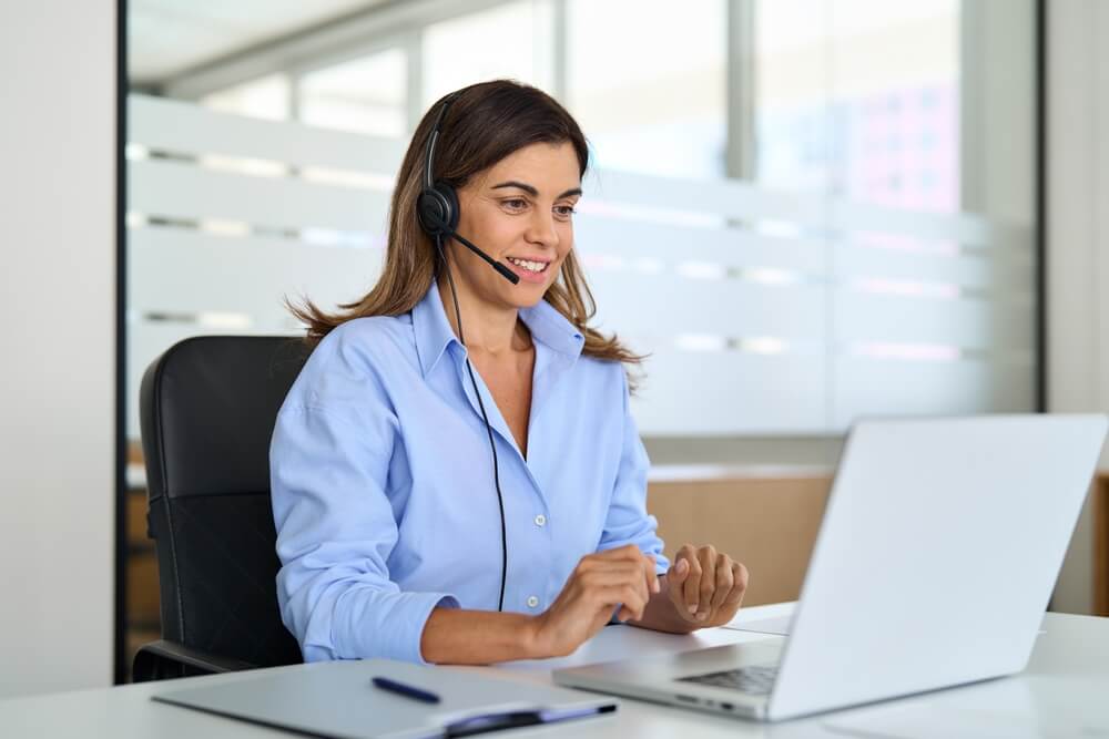 Busy middle aged female operator talking to patient sitting at desk