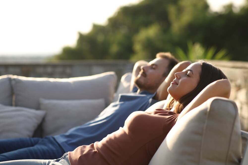 Relaxed couple resting sitting in an exterior sofa in a terrace
